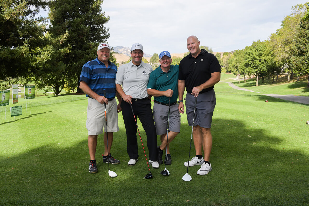 Four men play golf at a charity event